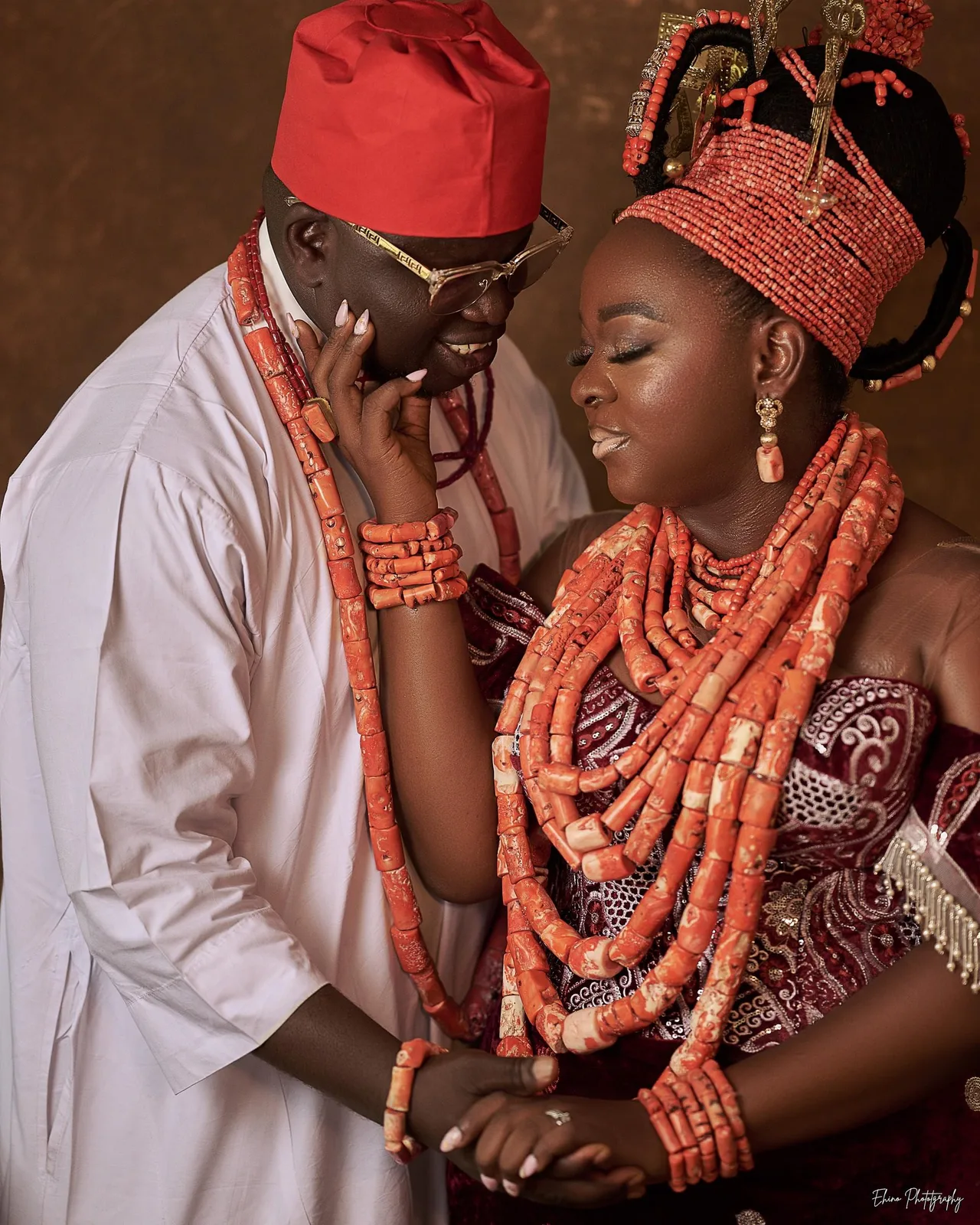 Bride and groom in coral beads and red caps holding hands at a traditional ceremony