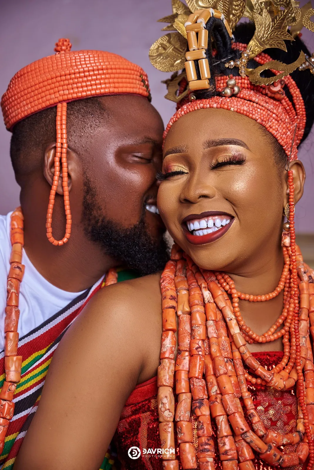 Edo traditional wedding couple in coral beads, the groom kissing the laughing bride's cheek